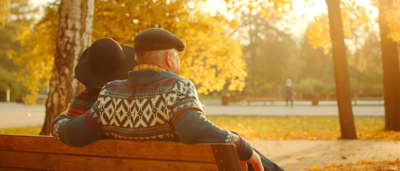 Eldre par sitter på en benk, i høstfarger