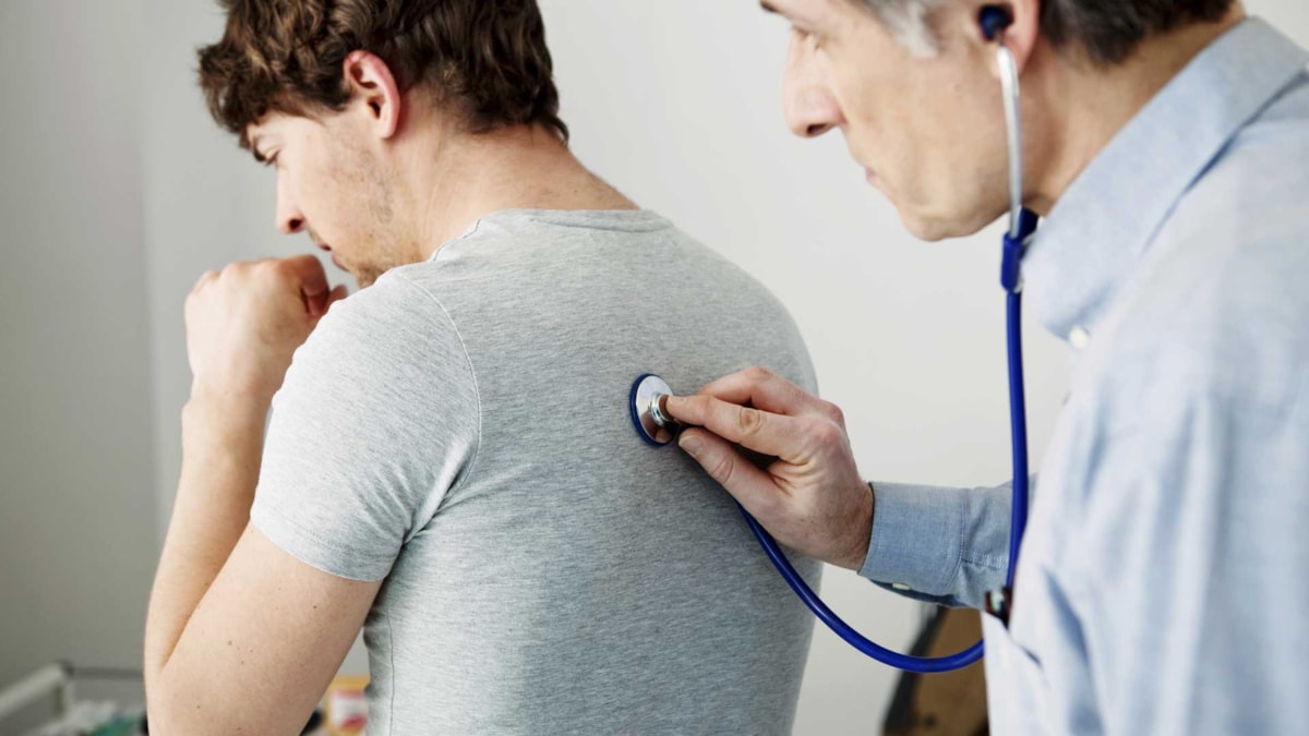 Lege som lytter på lungene til en mannlig pasient