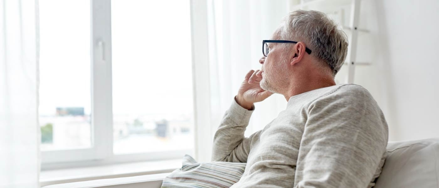 Mann som sitter i sofa og ser tenkefull ut av vinduet