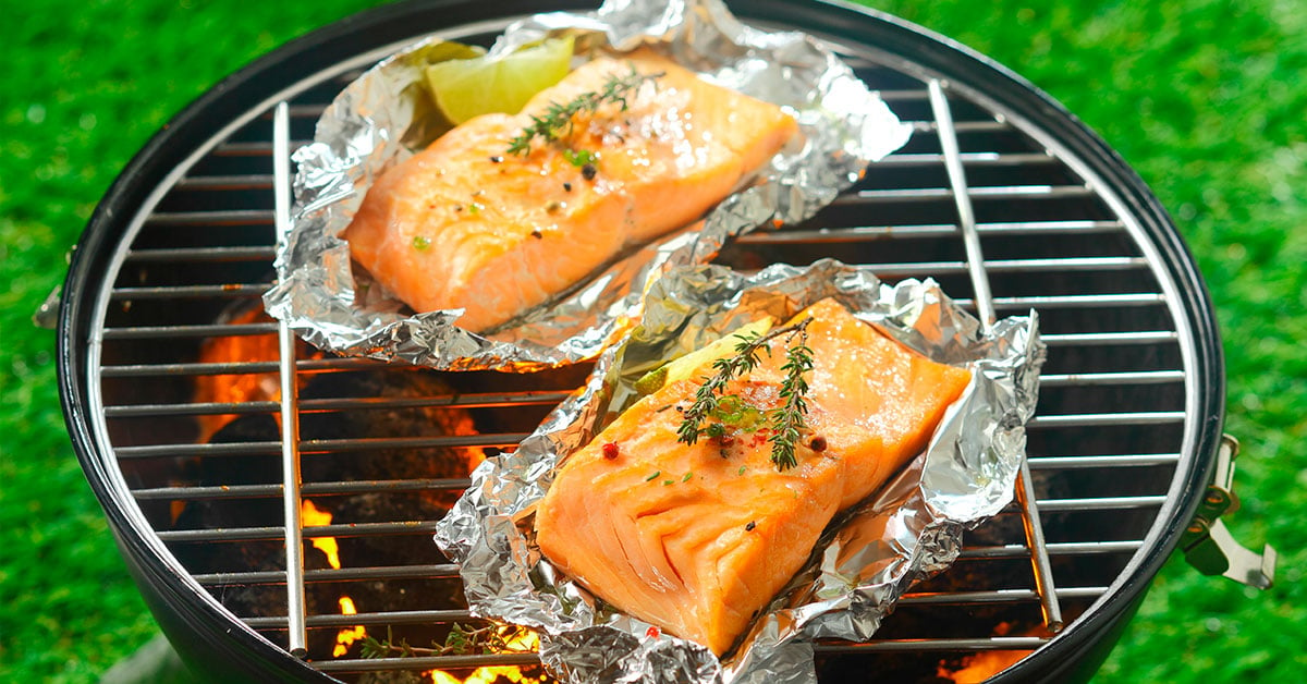 Bilde av en grill med to laksefileter på hvert sitt ark med aluminiumsfolie.